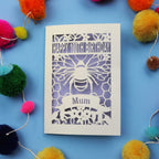 Laser-cut 100th birthday card for 'Mum' with bee design on a blue background with colourful pom-poms.