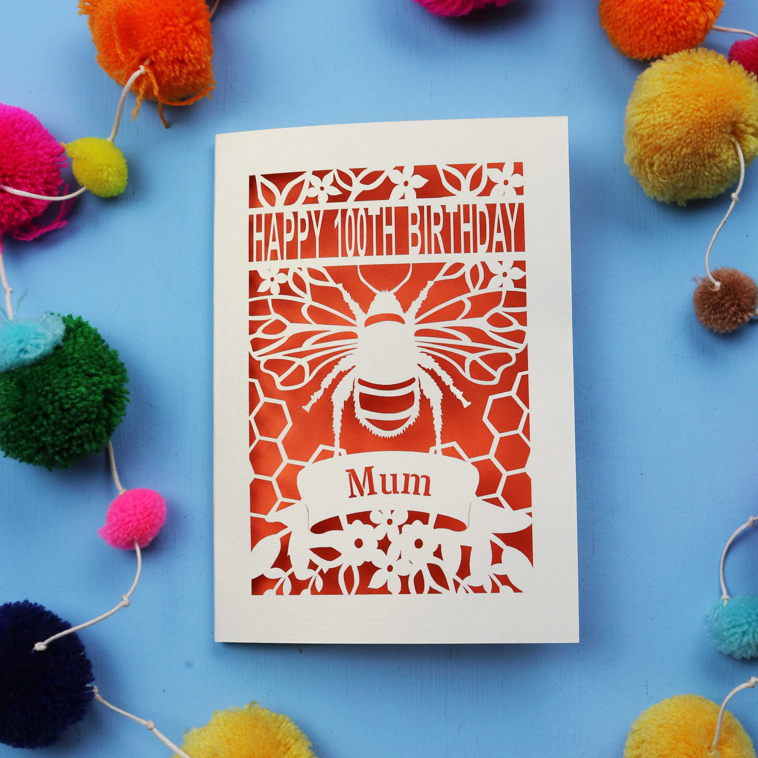 Laser-cut 100th birthday card for 'Mum' with bee design on a blue background with colourful pom-poms.