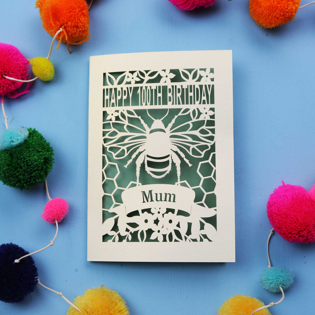 Laser-cut 100th birthday card for 'Mum' with bee design on a blue background with colourful pom-poms.