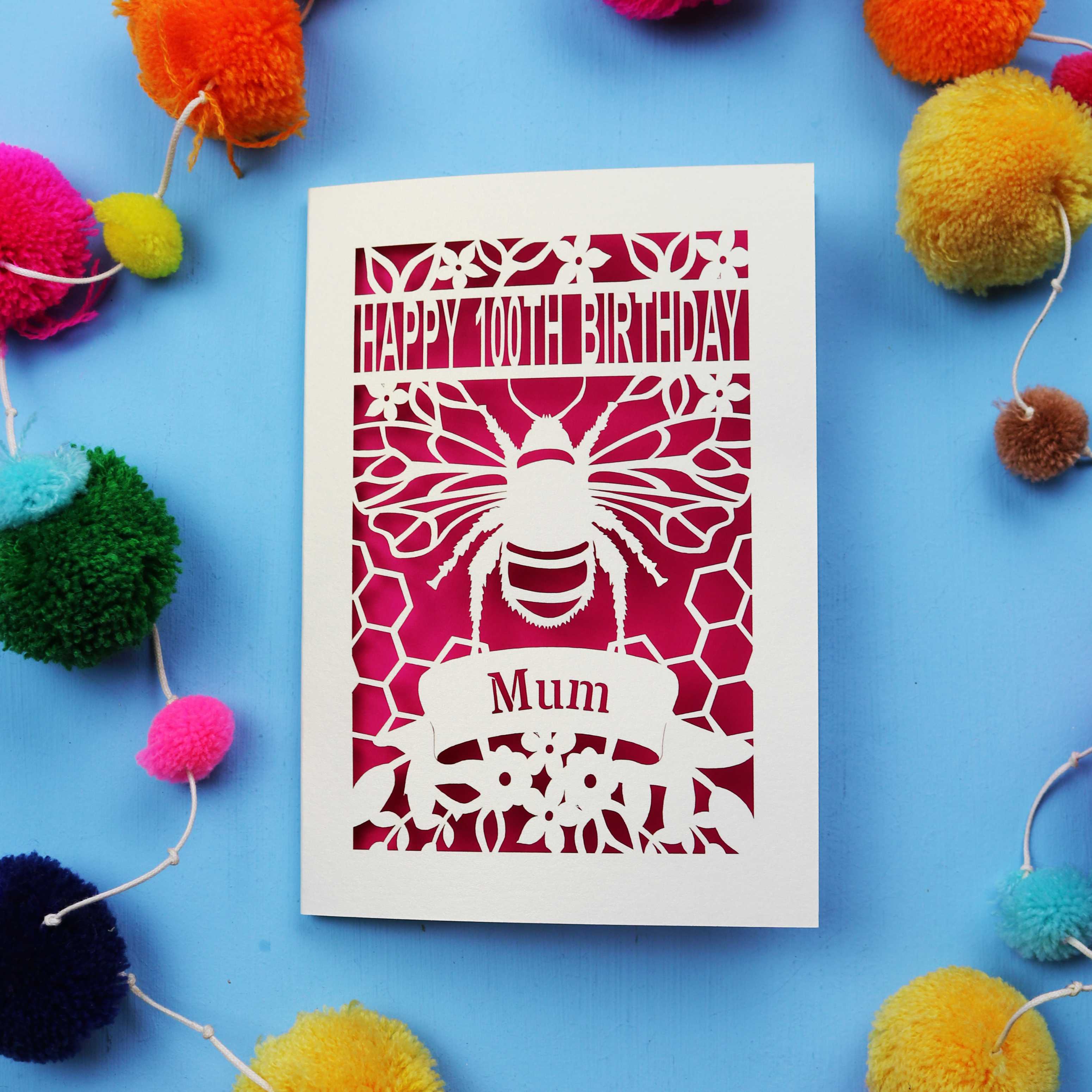 Laser-cut 100th birthday card for 'Mum' with bee design on a blue background with colourful pom-poms.
