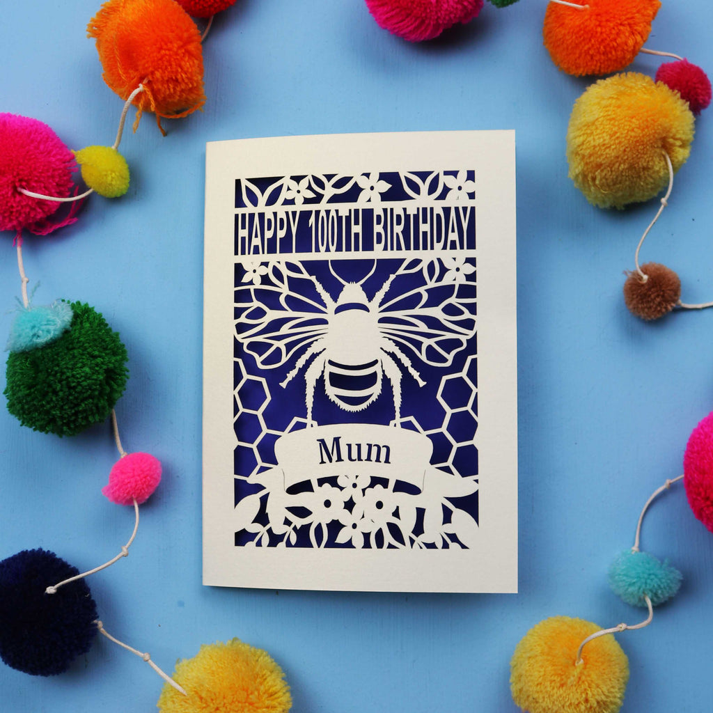 Laser-cut 100th birthday card for 'Mum' with bee design on a blue background with colourful pom-poms.