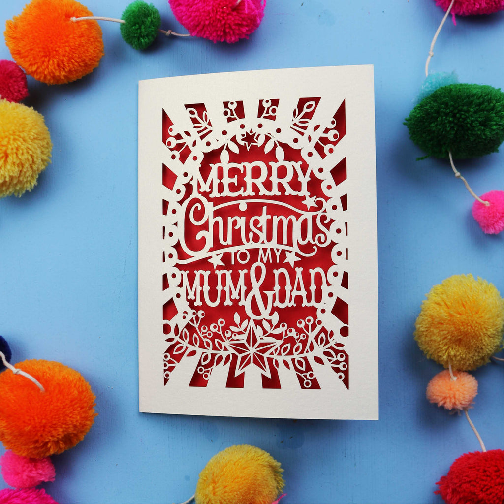 Laser cut Christmas card with 'Merry Christmas to my Mum & Dad' text on a blue background with colourful pom-poms.