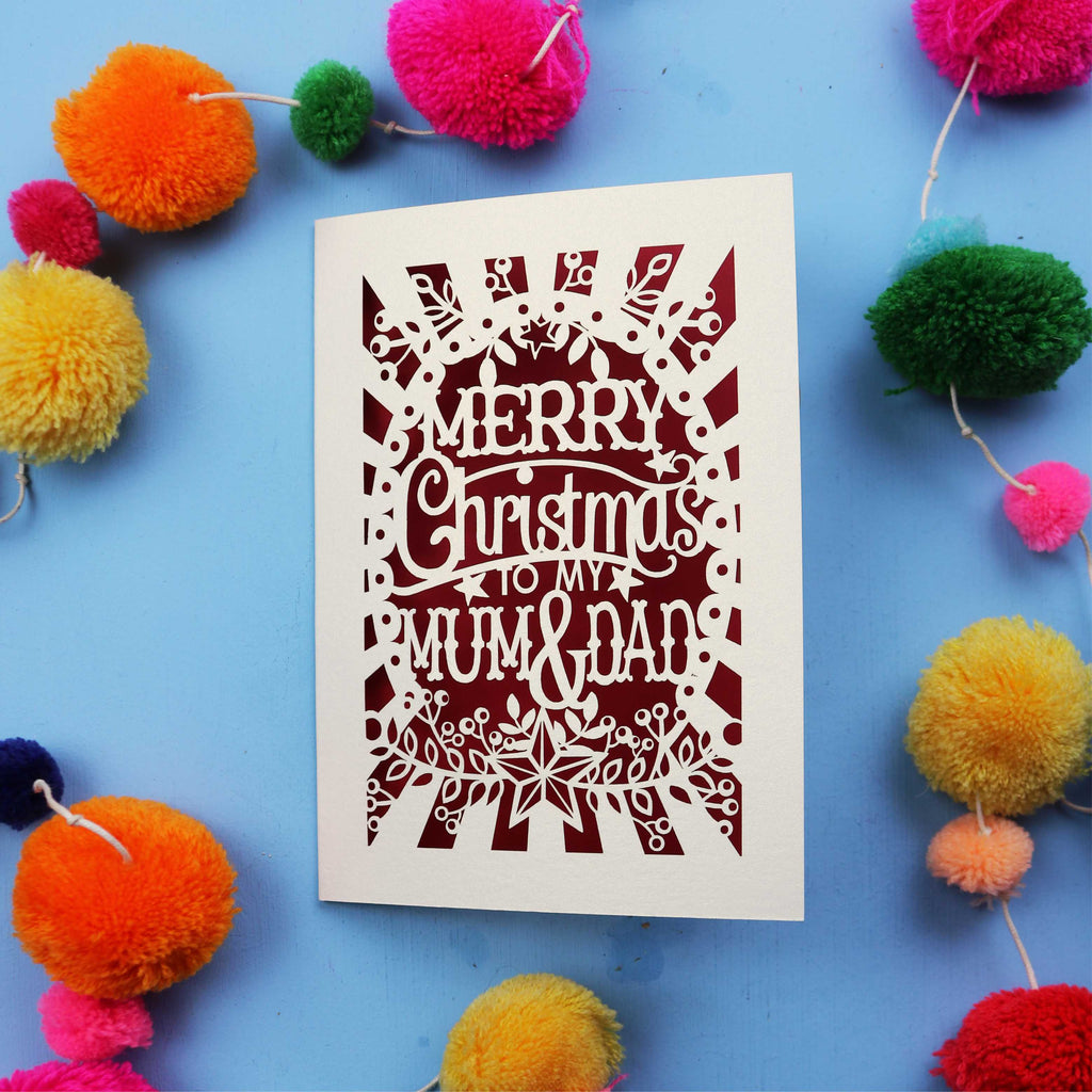 Laser cut Christmas card with 'Merry Christmas to my Mum & Dad' text on a blue background with colourful pom-poms.