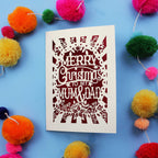Laser cut Christmas card with 'Merry Christmas to my Mum & Dad' text on a blue background with colourful pom-poms.