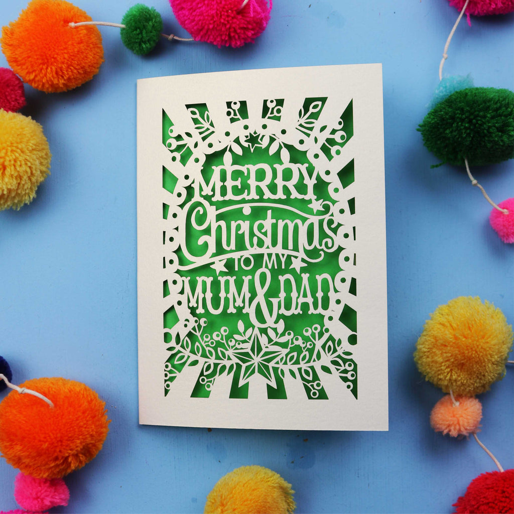 Laser cut Christmas card with 'Merry Christmas to my Mum & Dad' text on a blue background with colourful pom-poms.