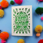 Laser cut Christmas card with 'Merry Christmas to my Mum & Dad' text on a blue background with colourful pom-poms.