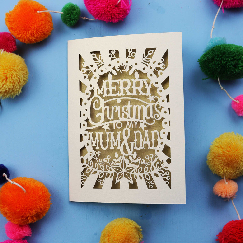 Laser cut Christmas card with 'Merry Christmas to my Mum & Dad' text on a blue background with colourful pom-poms.