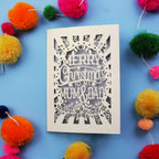 Laser cut Christmas card with 'Merry Christmas to my Mum & Dad' text on a blue background with colourful pom-poms.
