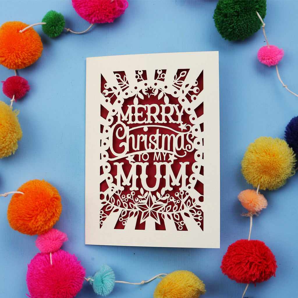 Christmas card with 'Merry Christmas to my Mum' text surrounded by colourful pom-poms on a blue background