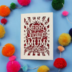 Christmas card with 'Merry Christmas to my Mum' text surrounded by colourful pom-poms on a blue background
