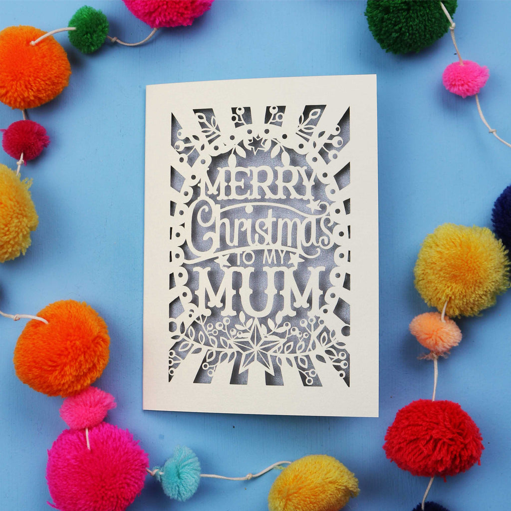 Laser Cut Mum Christmas card with 'Merry Christmas to my Mum' text on a blue background with colourful pom-poms.
