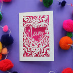 A laser cut mother's day card with the word "mum" inside a heart surrounded by floral shapes