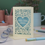A keepsake laser cut 'On your naming day' card, personalised with a name and date, standing on a desk with stationery items.