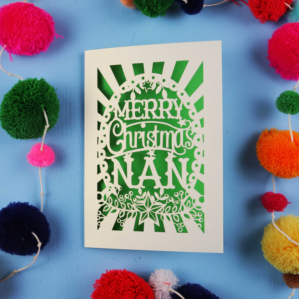 Christmas card with 'Merry Christmas Nan' text surrounded by colourful pom-poms on a blue background