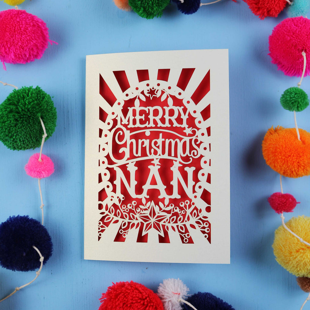Christmas card with 'Merry Christmas Nan' text surrounded by colourful pom-poms on a blue background