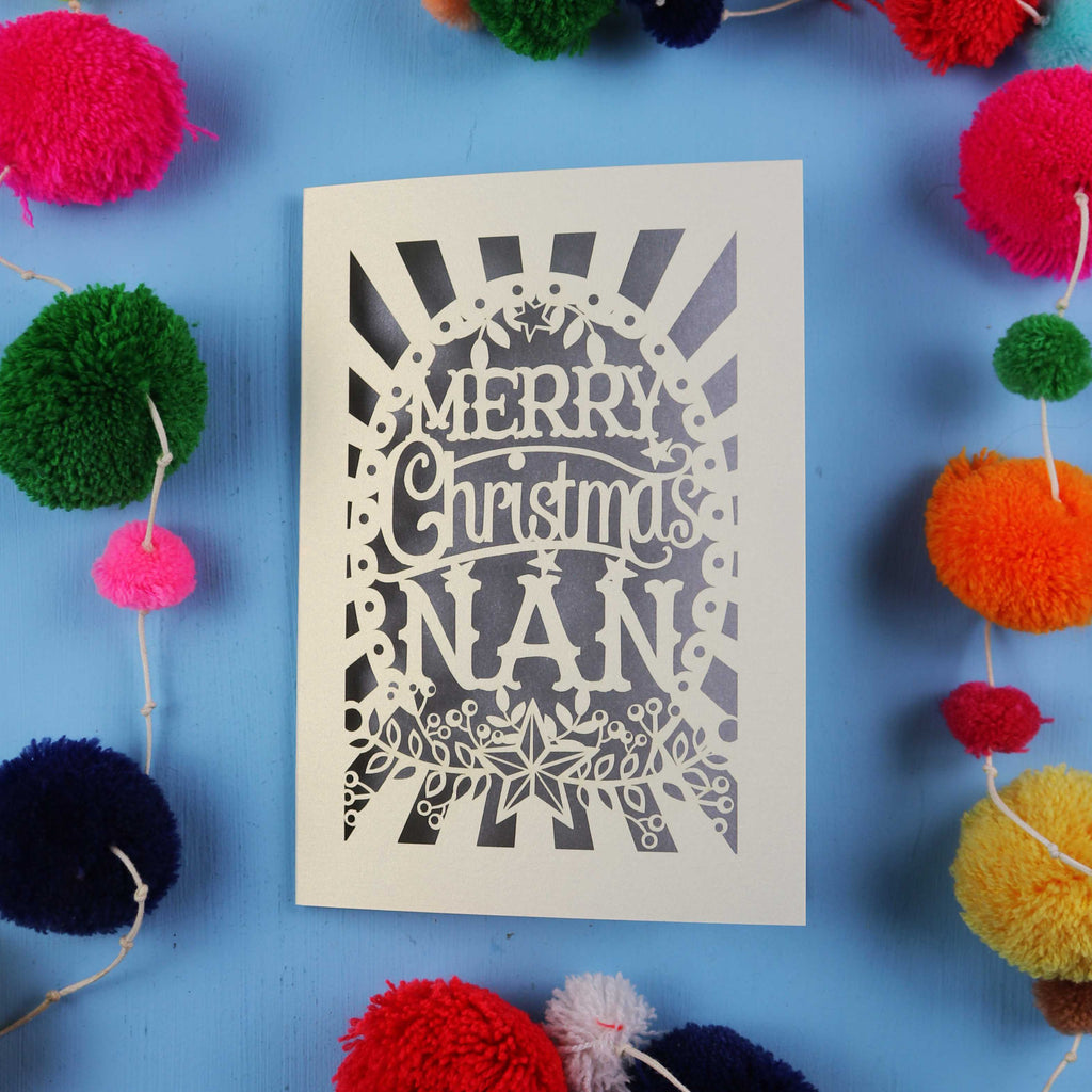 Christmas card with 'Merry Christmas Nan' text surrounded by colourful pom-poms on a blue background