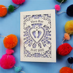 Personalised cut out baby card with personalised name and date, and intricate laser cut design on a blue background with colourful pom-poms.