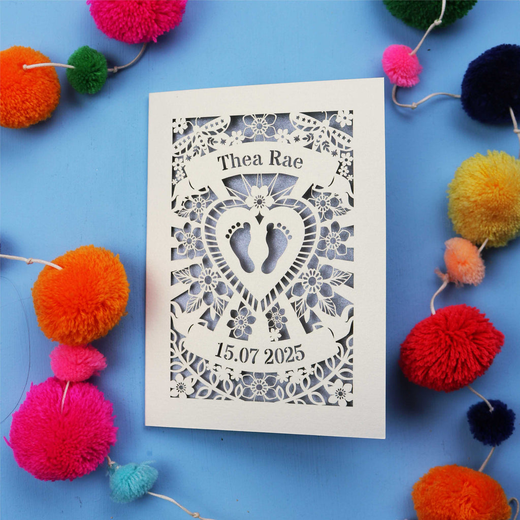 Unique Personalised baby card with personalised name and date, and intricate laser cut design on a blue background with colourful pom-poms.