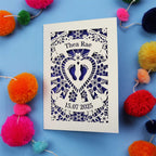 Keepsake Personalised baby card with personalised name and date, and intricate laser cut design on a blue background with colourful pom-poms.