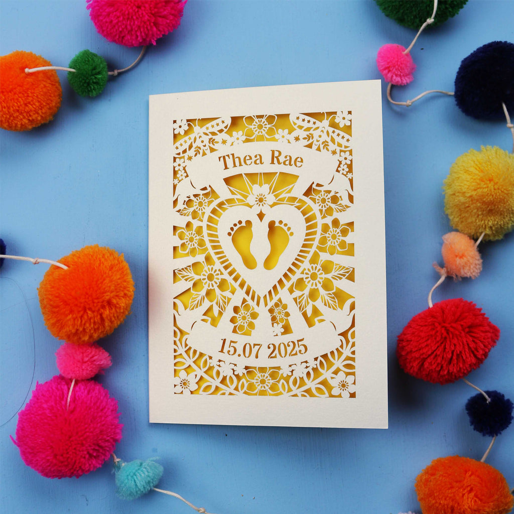 Personalised baby card with personalised name and date, and intricate laser cut design on a blue background with colourful pom-poms.