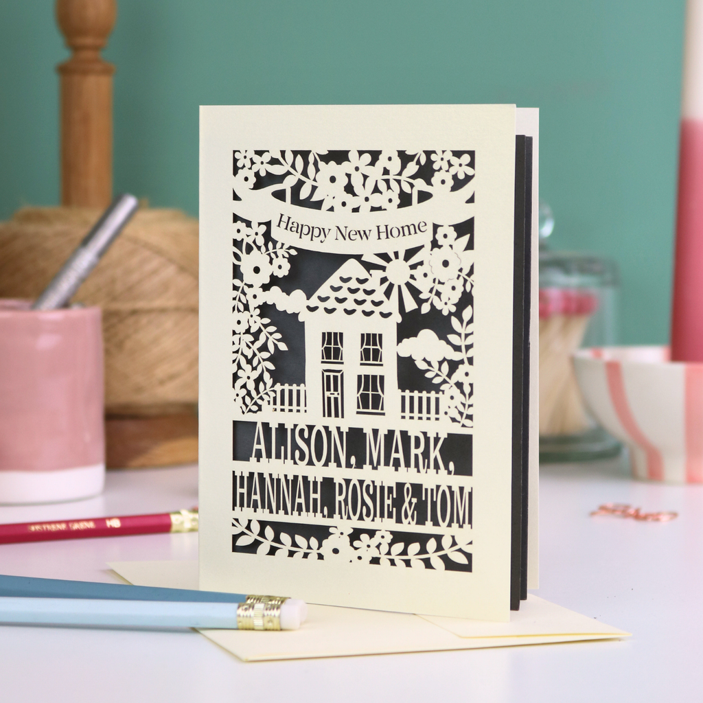 Laser-cut card with 'Happy New Home' text and house design on a table with stationery items.