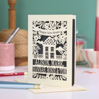Laser-cut card with 'Happy New Home' text and house design on a table with stationery items.