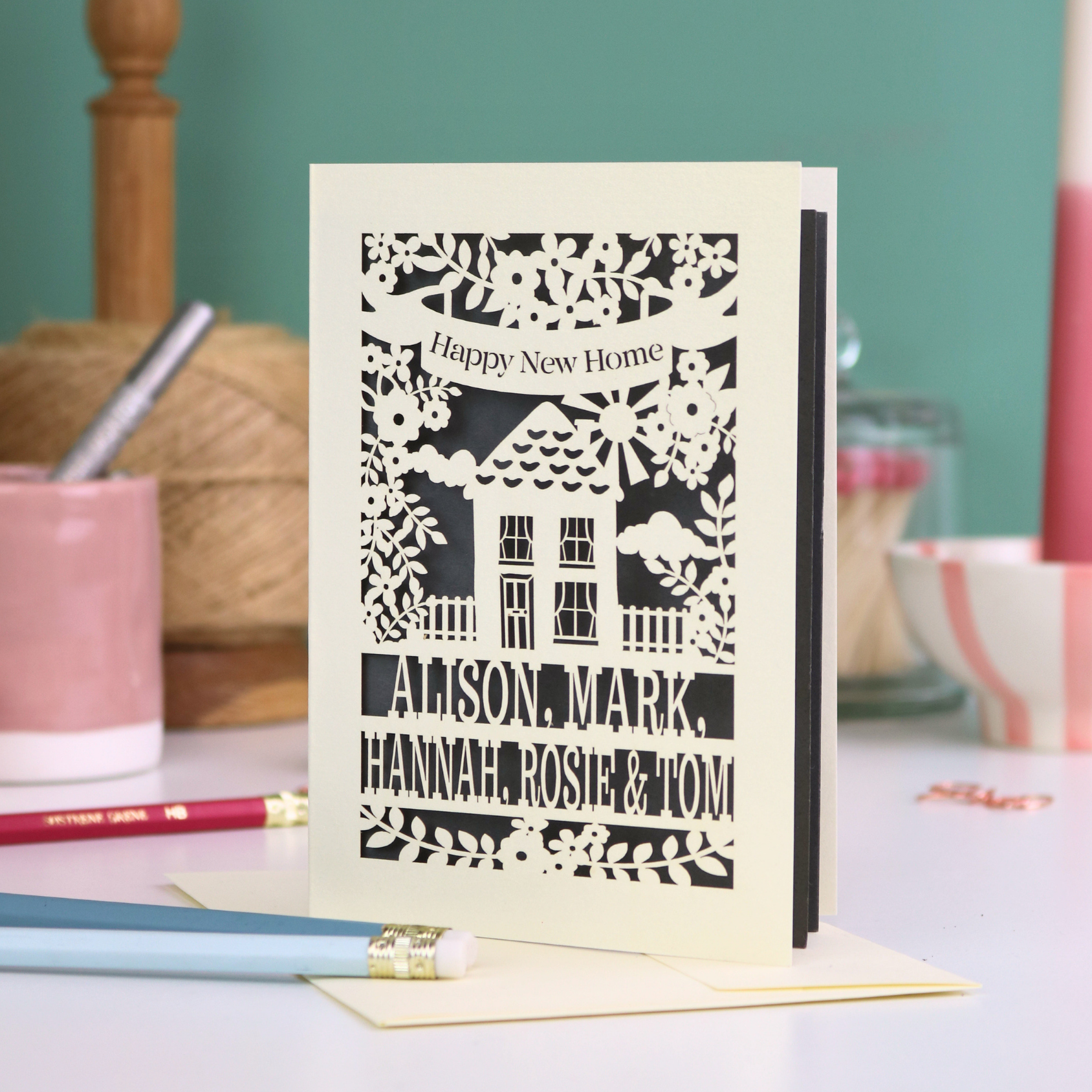 Laser-cut card with 'Happy New Home' text and house design on a table with stationery items.