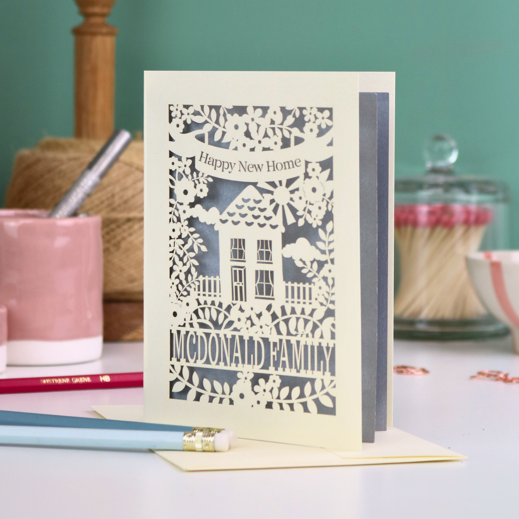Laser-cut 'Happy New Home' card with a house design on a table with stationery items.