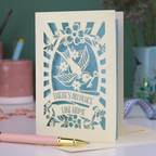 A laser cut new home card with cut out swallow design and text in a banner, "There's no place like home"