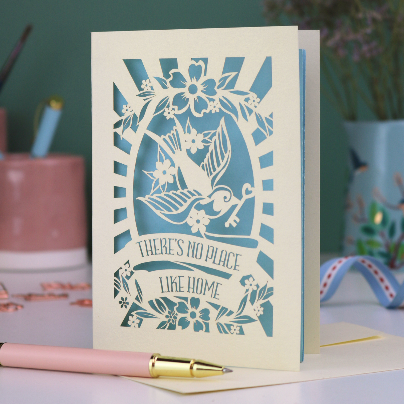 A laser cut new home card with cut out swallow design and text in a banner, "There's no place like home"