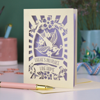 A laser cut new home card with cut out swallow design and text in a banner, "There's no place like home"