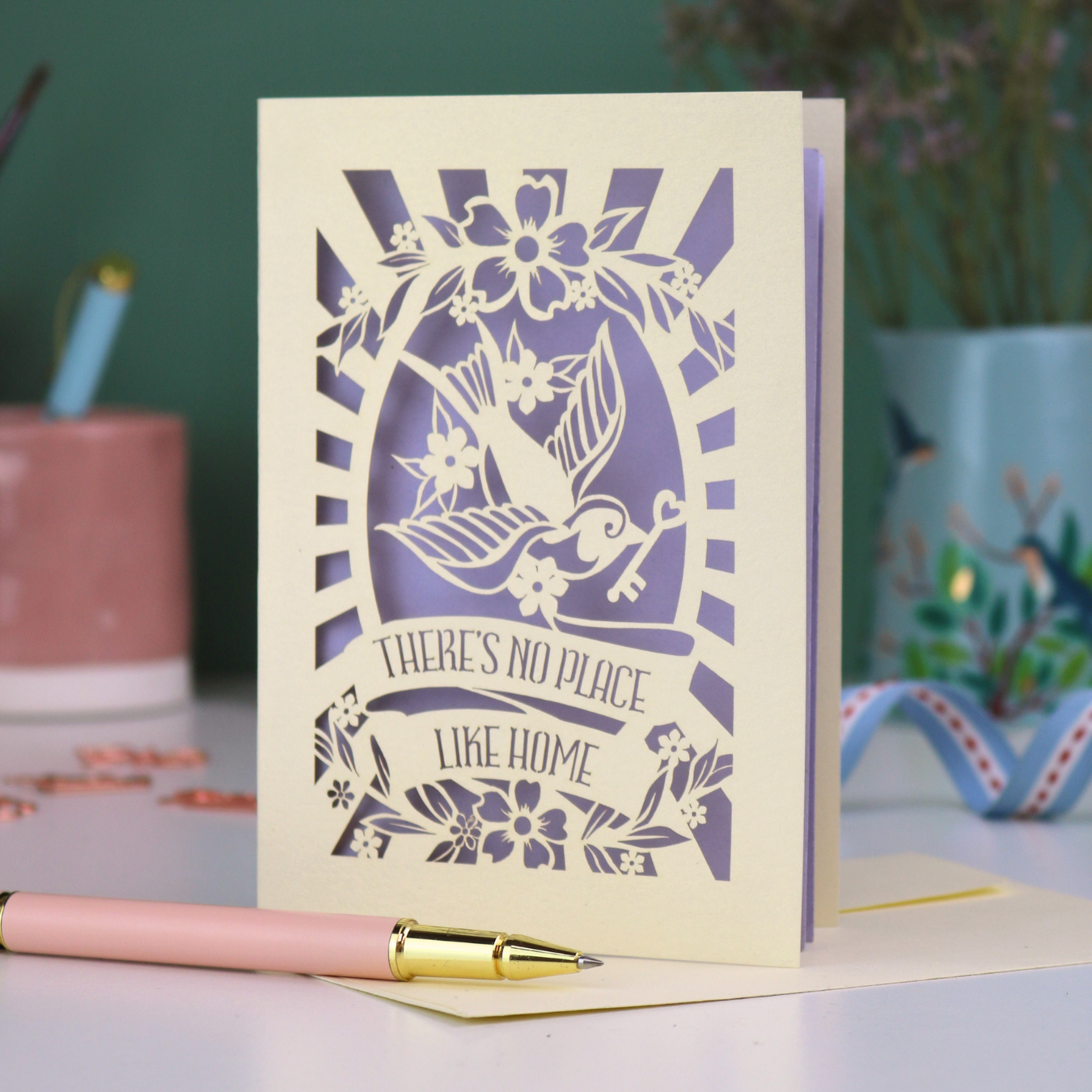 A laser cut new home card with cut out swallow design and text in a banner, "There's no place like home"