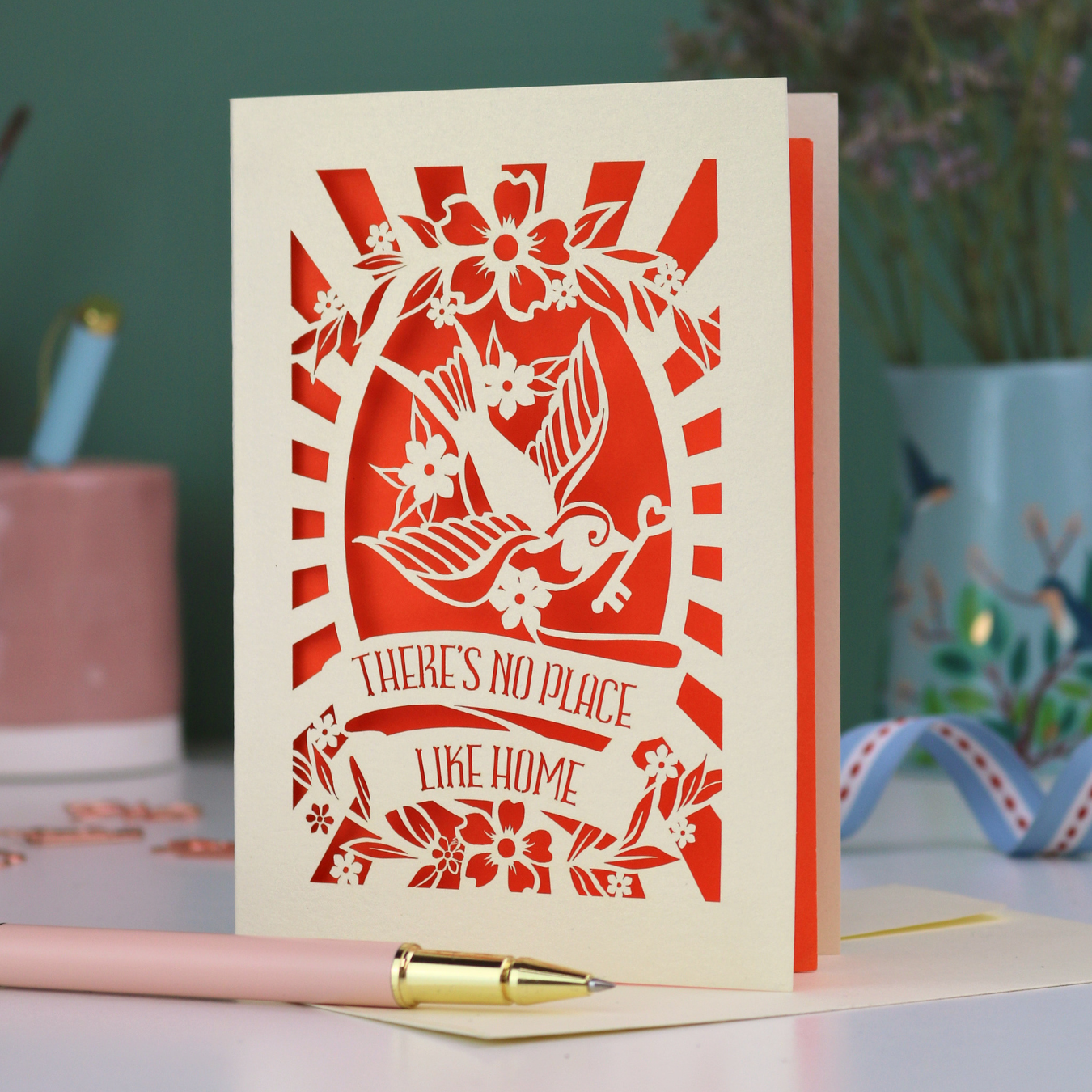 A laser cut new home card with cut out swallow design and text in a banner, "There's no place like home"