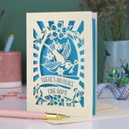 A laser cut new home card with cut out swallow, key and flower design and text in a banner, "There's no place like home"