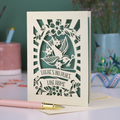 A laser cut new home card with cut out swallow design and text in a banner, "There's no place like home"