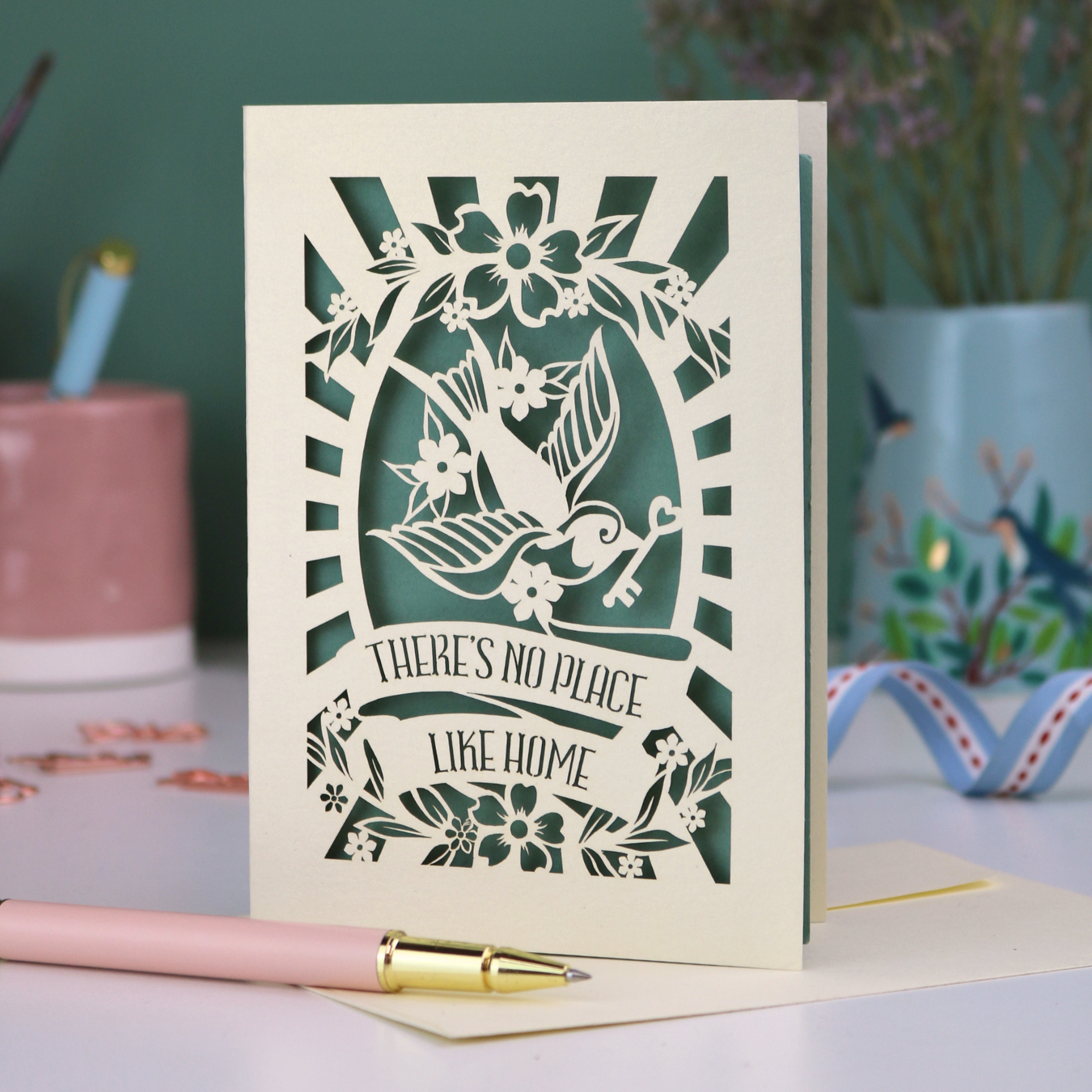 A laser cut new home card with cut out swallow design and text in a banner, "There's no place like home"