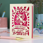 A laser cut new home card with cut out swallow and key design and text in a banner, "There's no place like home"