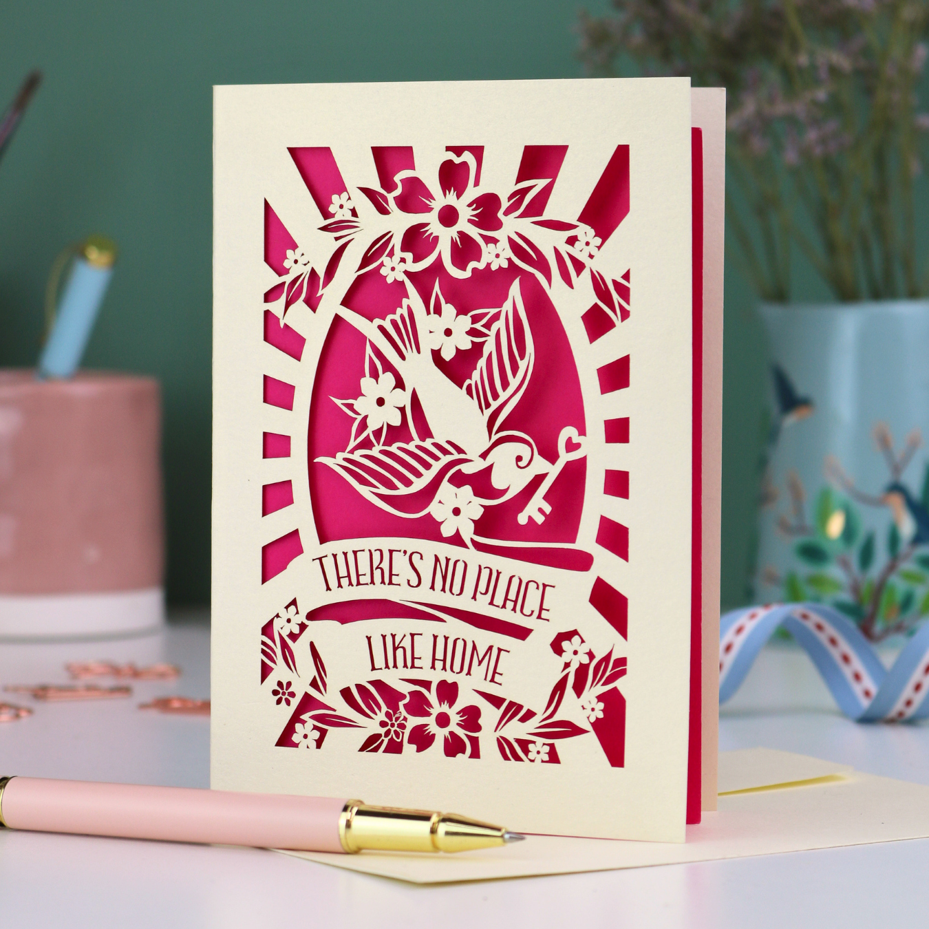 A laser cut new home card with cut out swallow and key design and text in a banner, "There's no place like home"