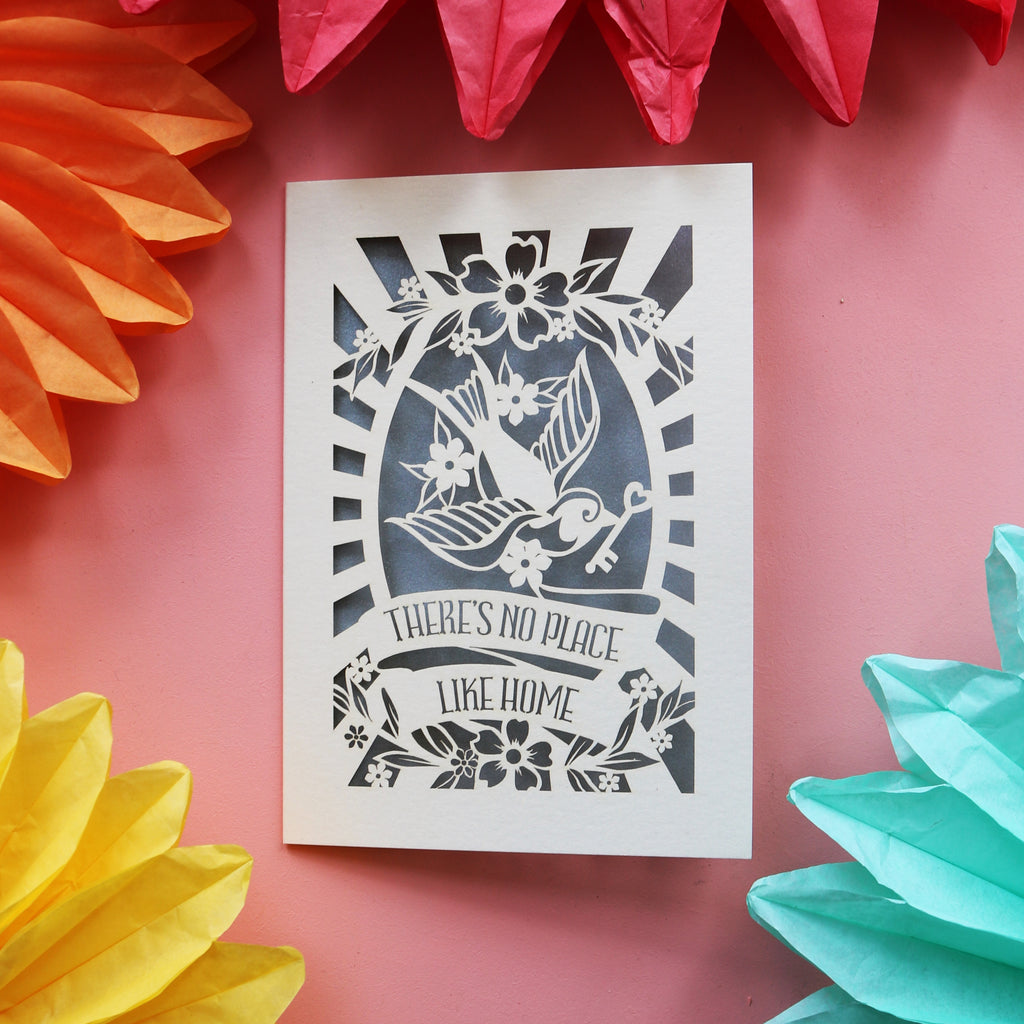 A cut out house warming card featuring a bird holding a key and the words "There's no place like home."