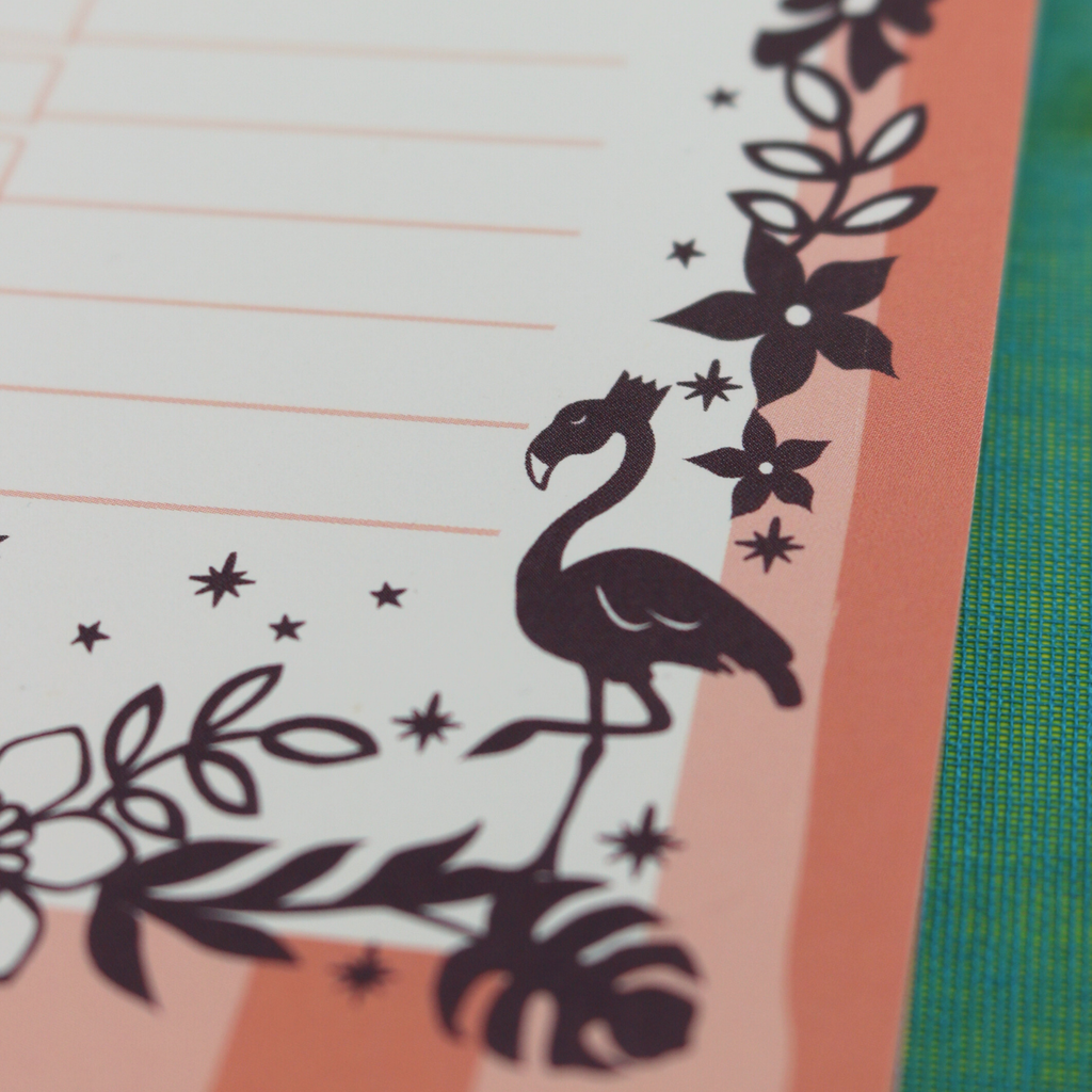 A close up detail of a notepad with pink striped border and purple floral flamingo illustrations
