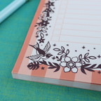 A close up detail of a notepad with pink striped border and purple floral illustrations