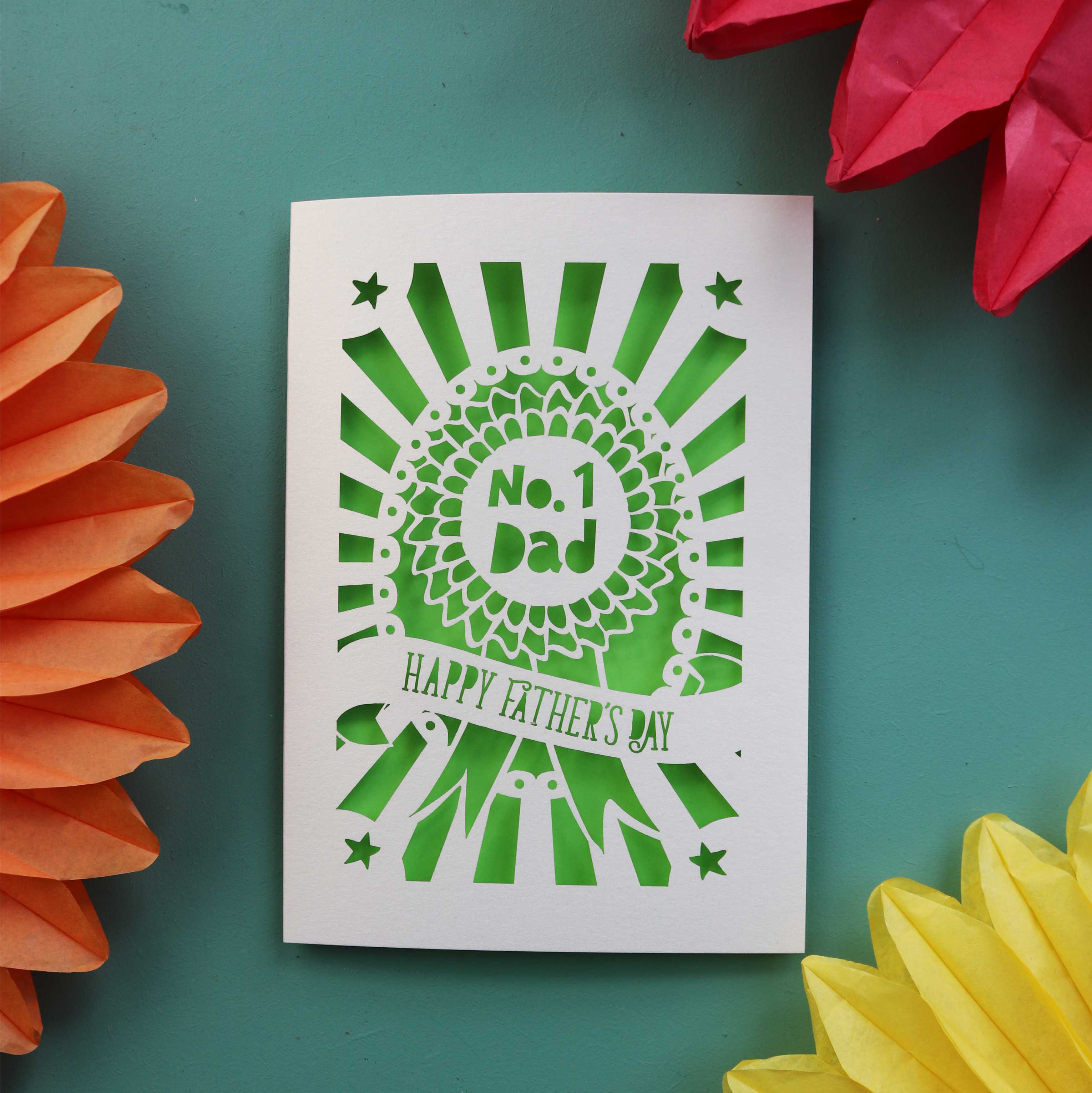 A laser cut father's day card with a rosette and banner, and a sunbeam border