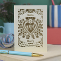 Personalised laser cut anniversary card with decorative text and floral heart design on a table with stationery items.