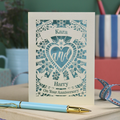 Personalised laser cut anniversary card with decorative text and floral heart design on a table with stationery items.