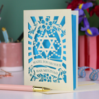 Bar Mitzvah card with blue and cream design on a desk with stationery items.