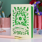 Bar Mitzvah card with green Star of David design on a desk with stationery items.