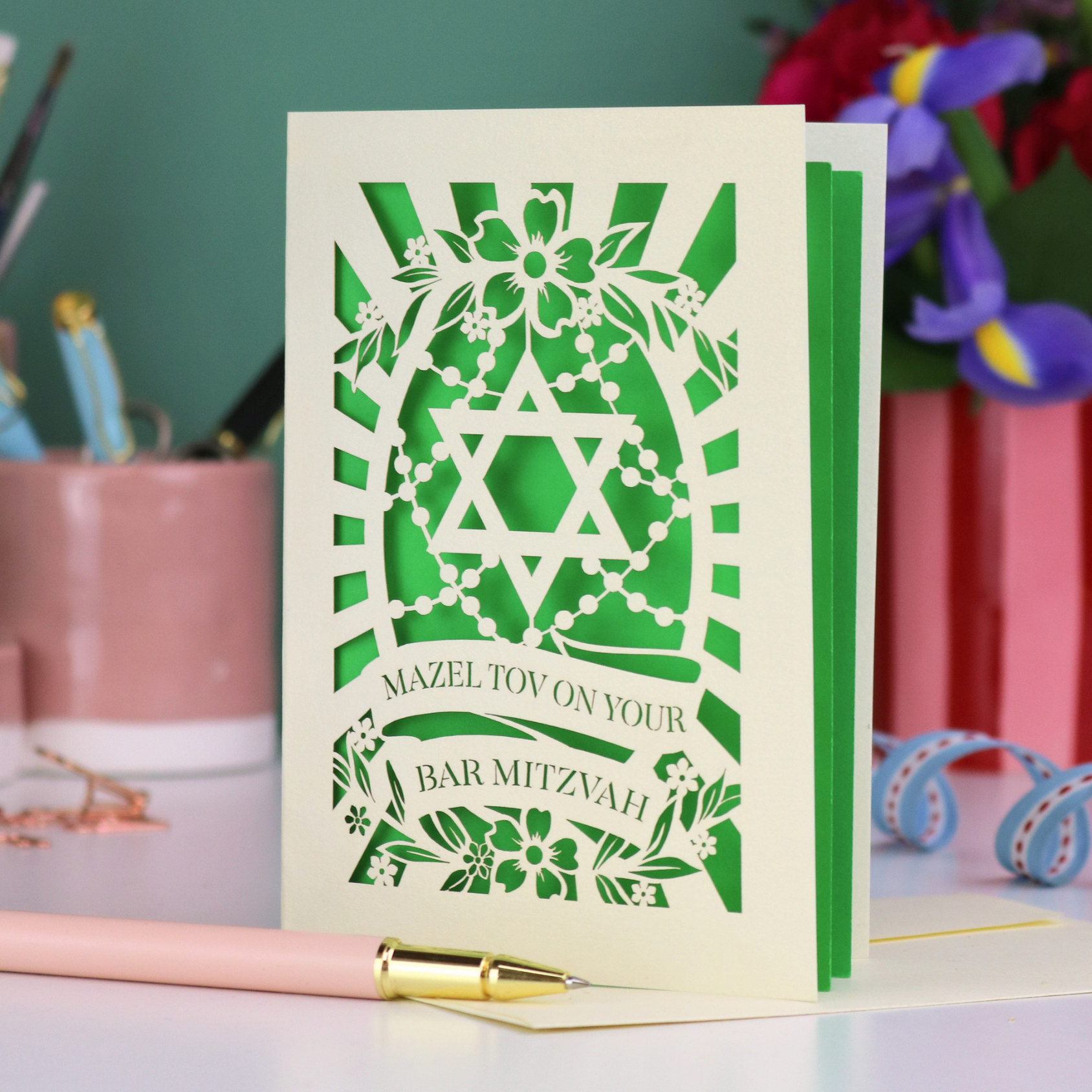 Bar Mitzvah card with green Star of David design on a desk with stationery items.