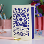 Bar Mitzvah card with blue and white design on a desk with stationery items.