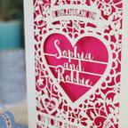 A cream laser cut engagement card on a desk with stationery items. The card is portrait-orientation, with floral cut out details and 'Congratulations, name and name, on your engagement'