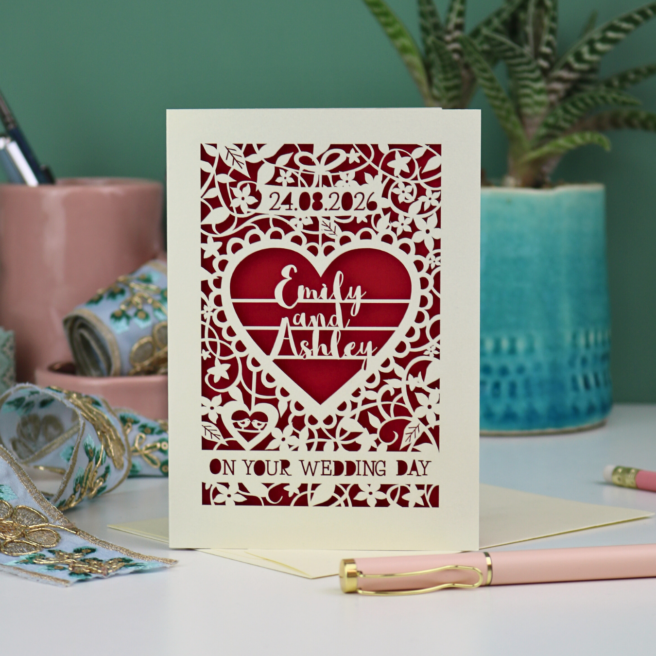 Laser cut Wedding card with decorative heart design and text on a table with stationery items.